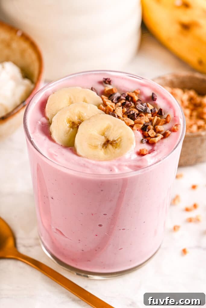 A creamy strawberry cottage cheese smoothie in a glass, topped with banana slices and crunchy cacao nibs.