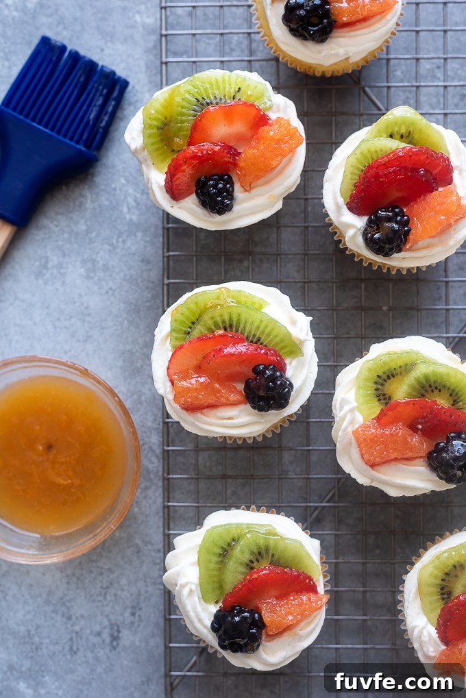 Decorated vanilla cupcakes with fruit and whipped cream frosting.