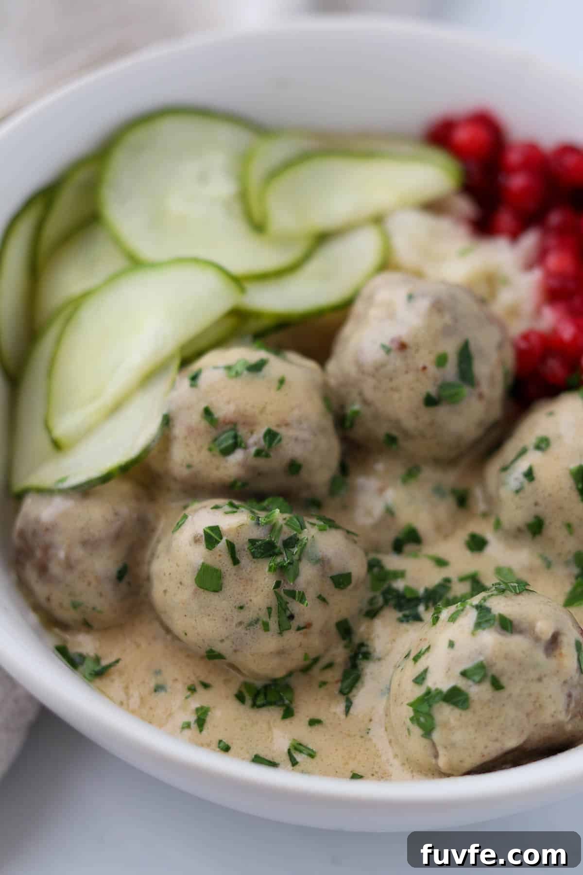 Swedish Meatballs with Classic Creamy Gravy (Köttbullar) 15 Close up of Swedish Meatballs with Gravy and pickles and lingonberries.