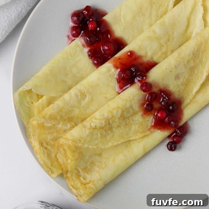 Close up of 3 Swedish pancakes on a plate topped with lingonberries.