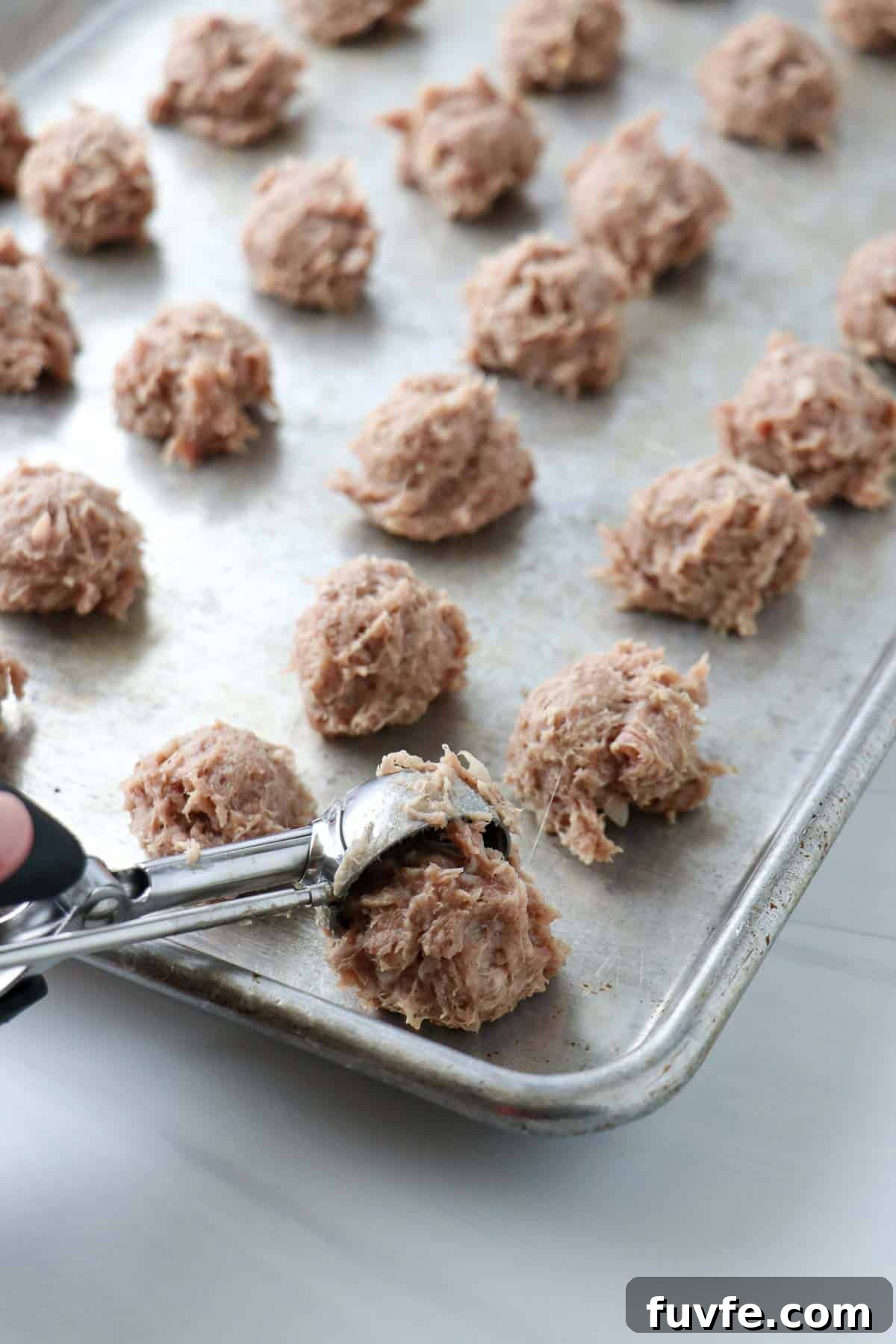 Swedish Meatballs with Classic Creamy Gravy (Köttbullar) 9 Person dropping tablespoons of meatball mix onto a baking sheet.