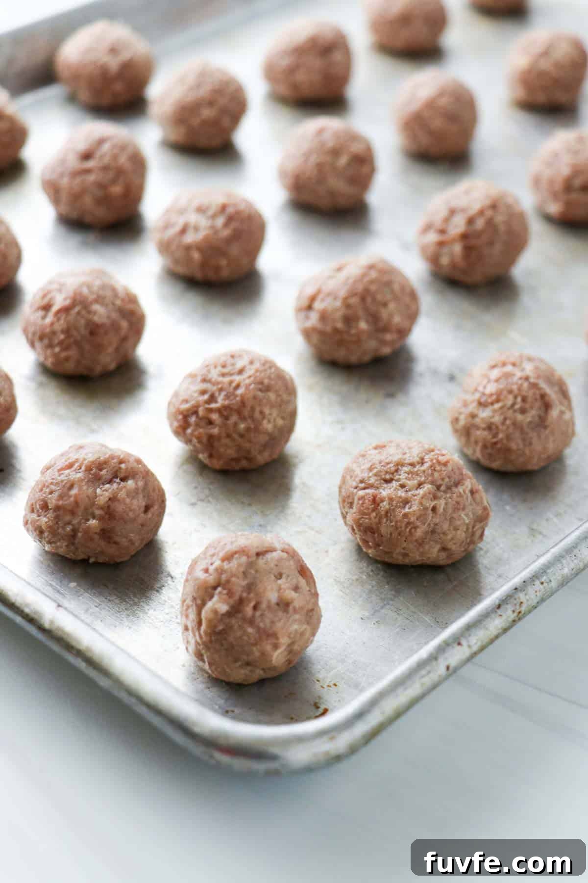 Swedish Meatballs with Classic Creamy Gravy (Köttbullar) 10 Uncooked, rolled Swedish Meatballs on a baking sheet.
