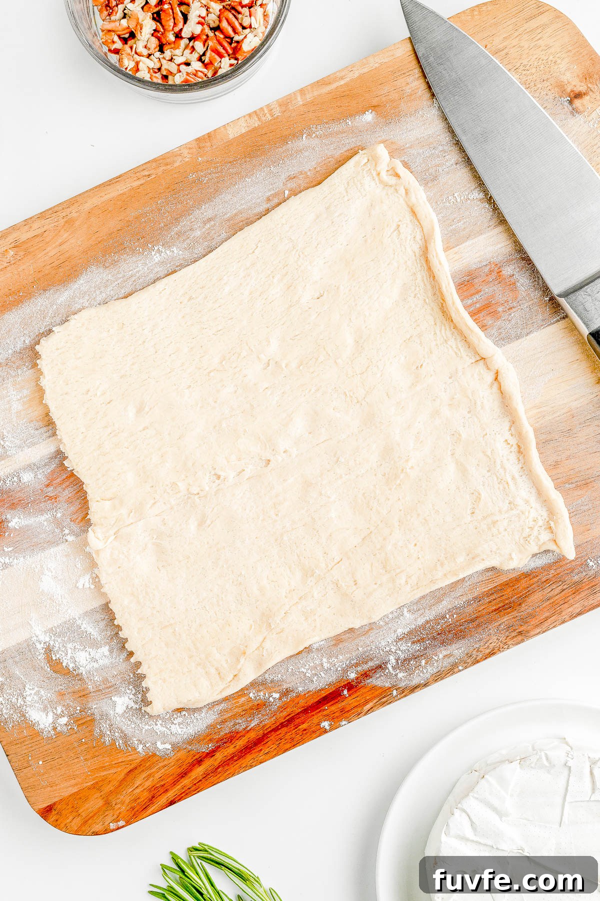 Raw crescent roll dough spread out on a wooden cutting board next to a knife. 