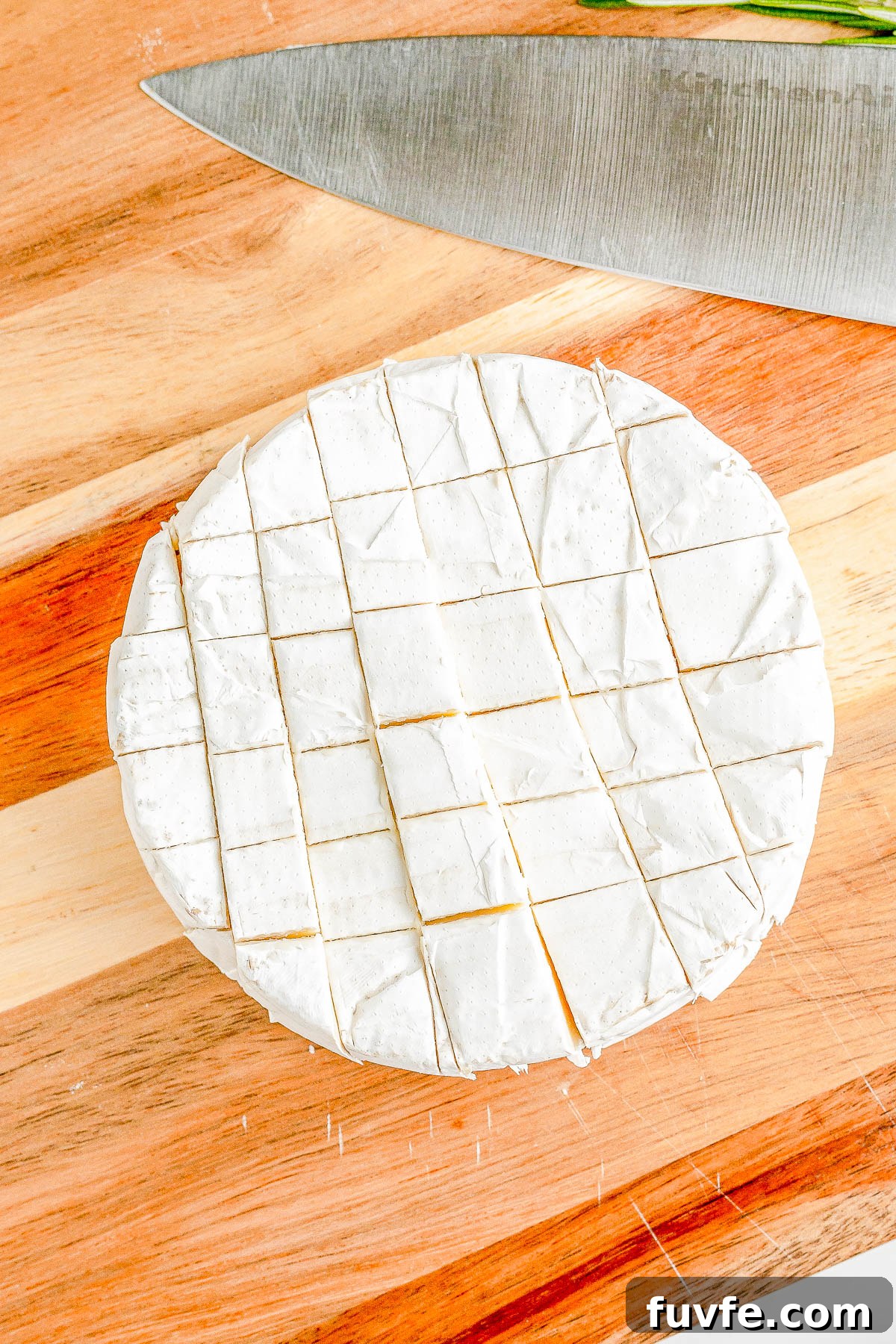 A wheel of brie sliced into bite-sized pieces on a wooden cutting board next to a knife. 