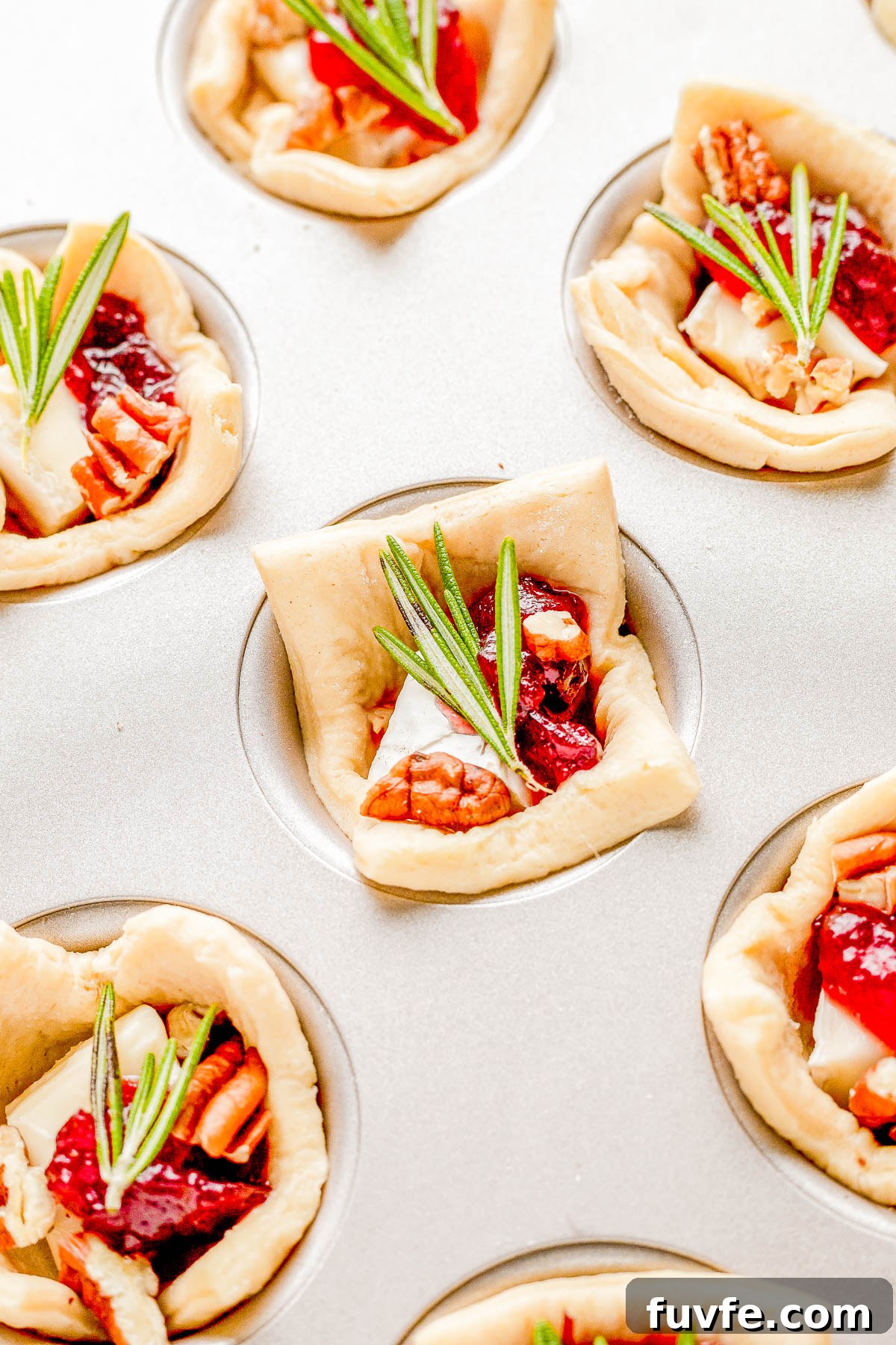 Raw cranberry brie bites topped with pecans and fresh rosemary in a muffin cup.