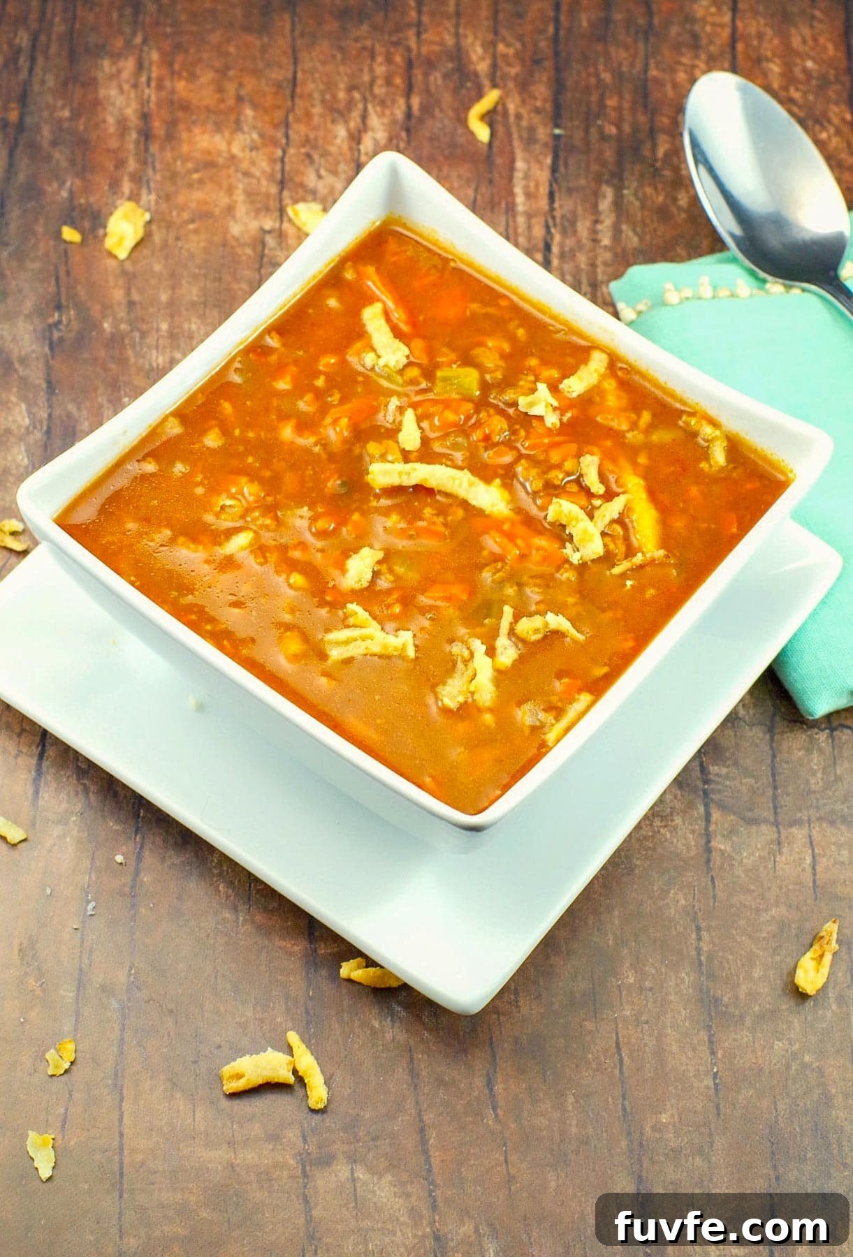 Award-Winning Shredded Carrot Chowder Recipe 10 healthy carrot soup in a white bowl, on a white plate, on brown faux wooden surface, with pastel green napkin on right side and crispy onions on soup and scattered on surface