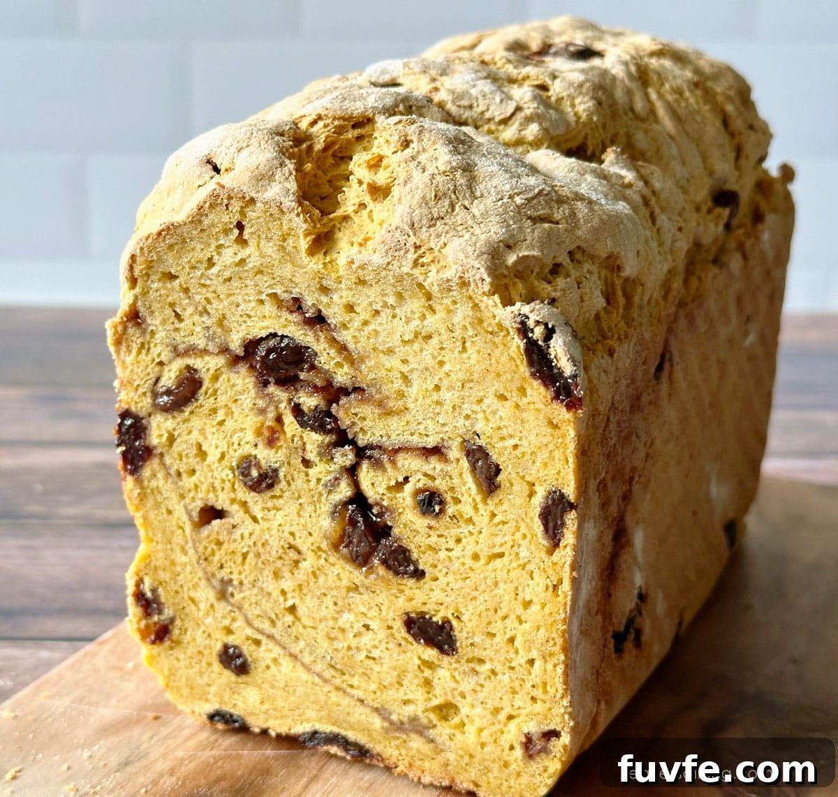 Gluten-Free Pumpkin Sandwich Bread with Cinnamon Swirl 11 The front of a loaf of a yeasted gluten-free pumpkin raisin bread on a wooden cutting board.