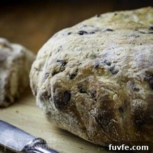 Side view of whole loaf of olive bread on a wooden cutting board with a butter knife on the side.