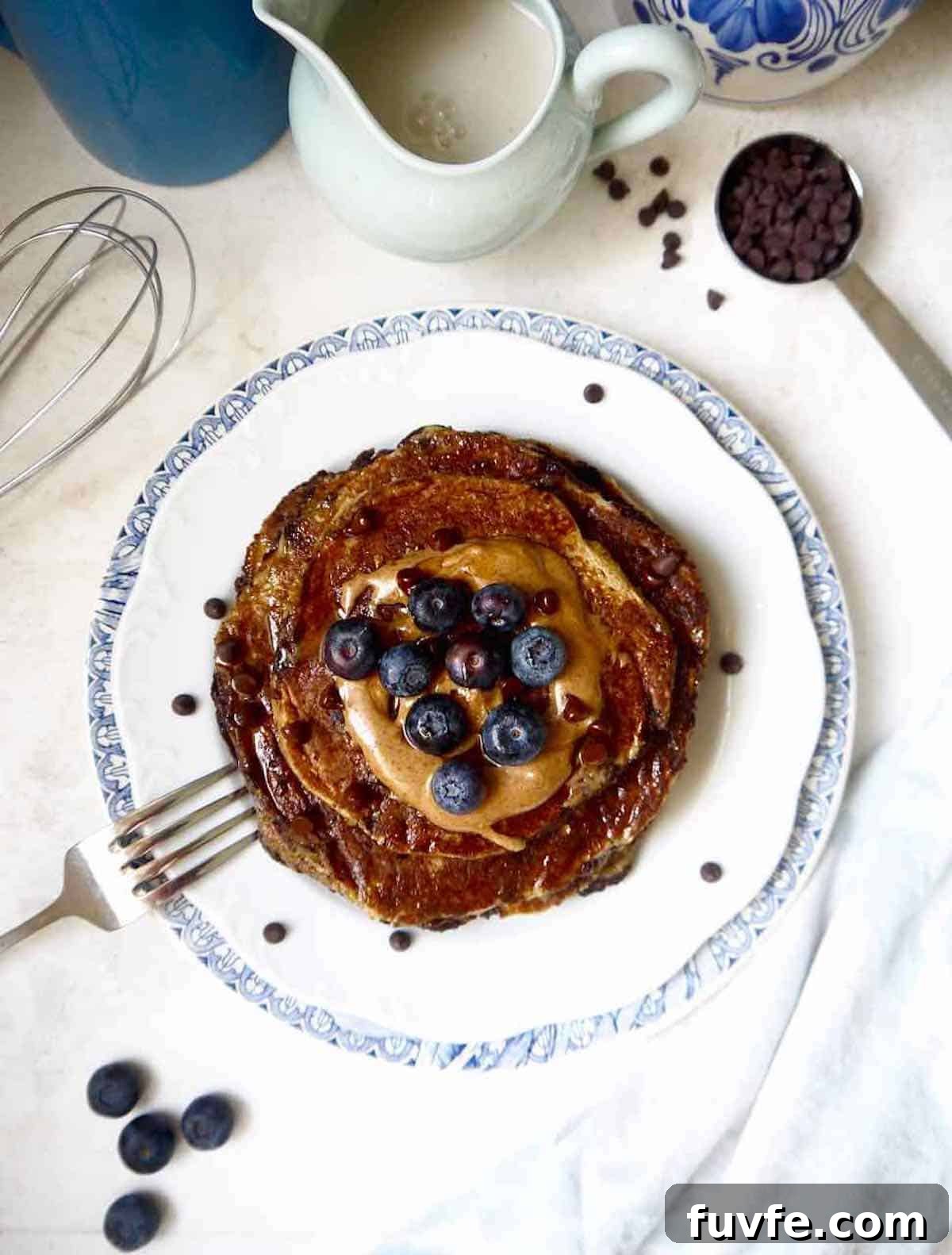Healthy banana pancakes recipe on a plate with blueberries, and almond butter on top.