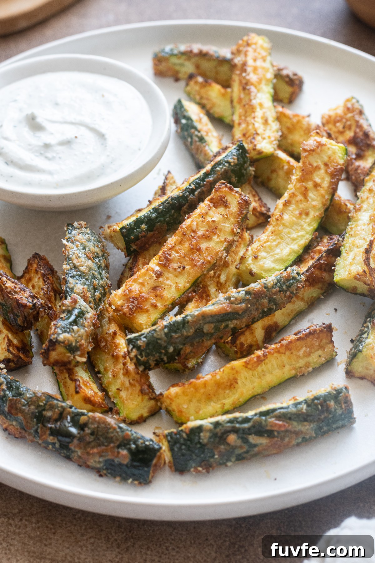 Golden brown air fryer zucchini fries coated in parmesan cheese with a side of Greek yogurt ranch.