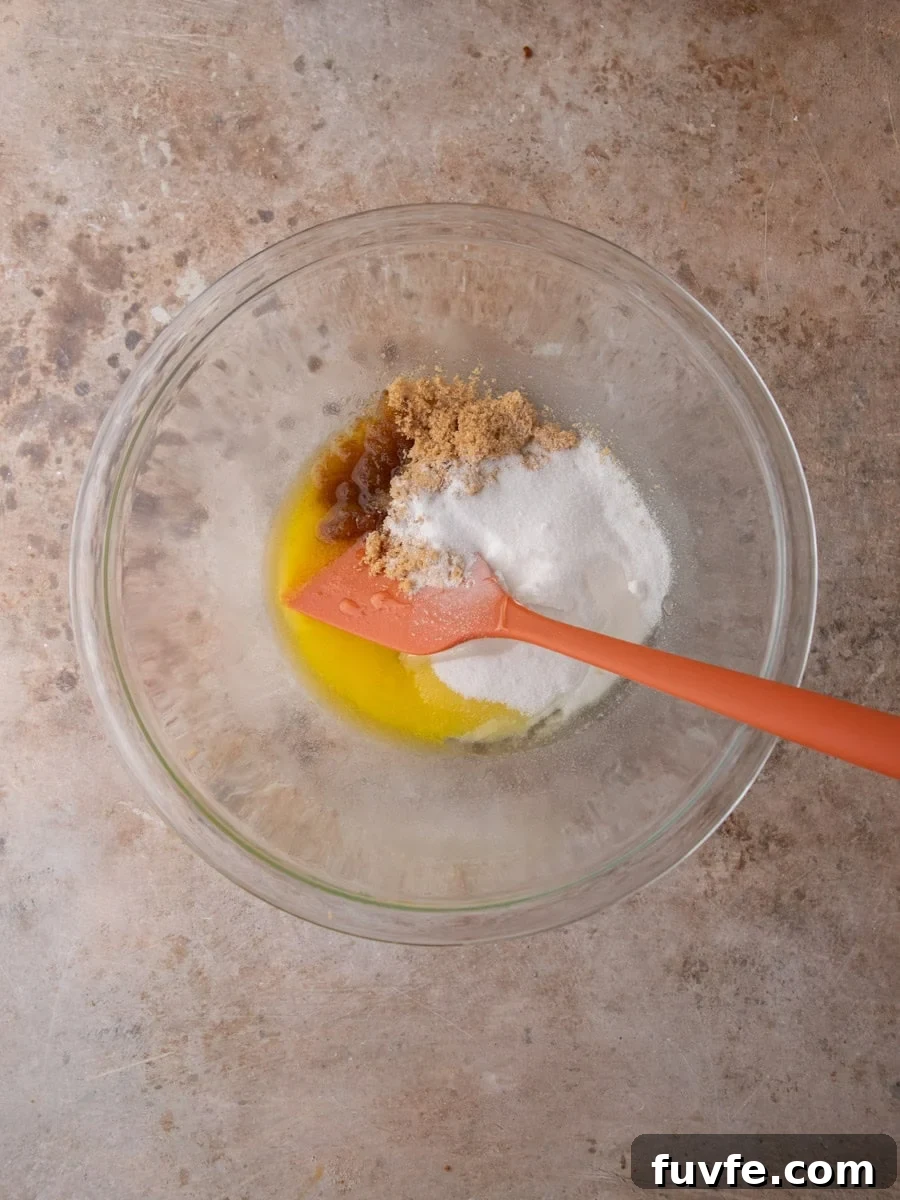 Melted butter, brown sugar, and granulated sugar combined in a glass bowl to start cookie dough.