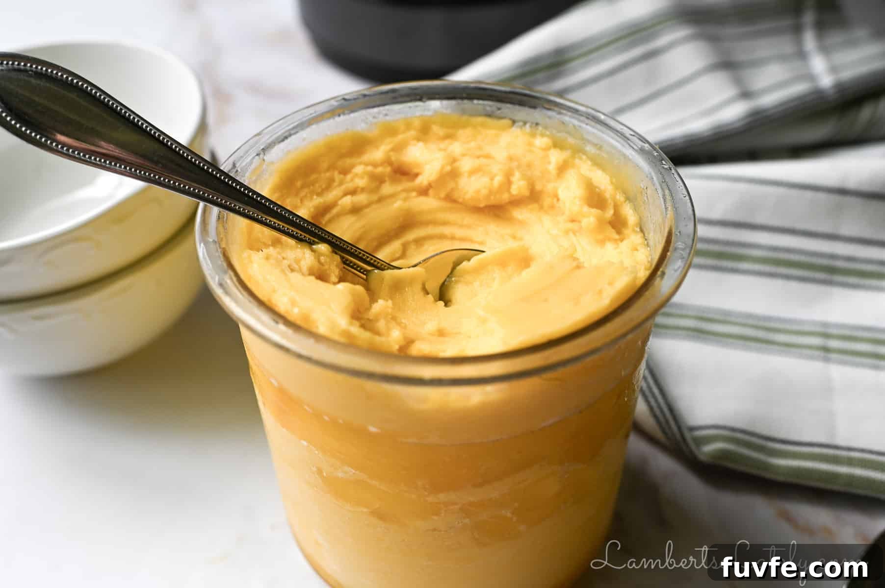 2-Ingredient Mango Sorbet Recipe for Ninja Creami Machines 2 pint container of ninja creami mango sorbet with a spoon in it, napkin, stack of bowls.