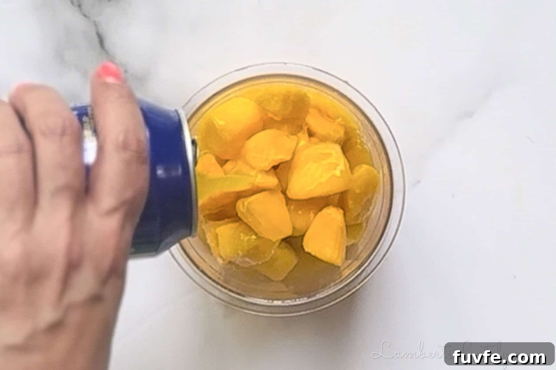 2-Ingredient Mango Sorbet Recipe for Ninja Creami Machines 6 Pouring canned mango nectar into a plastic Ninja Creami pint over frozen fruit pieces.