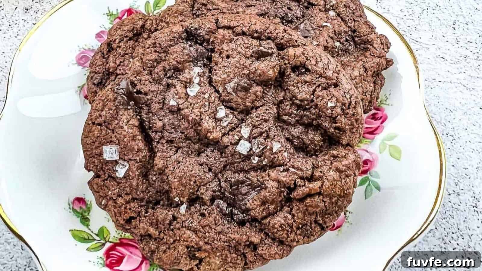 29 Christmas Baking Ideas for Home Bakers Who Love a Busy Oven 18 A close-up of a large chocolate cookie sprinkled with coarse salt, placed on a decorative plate with pink rose patterns.
