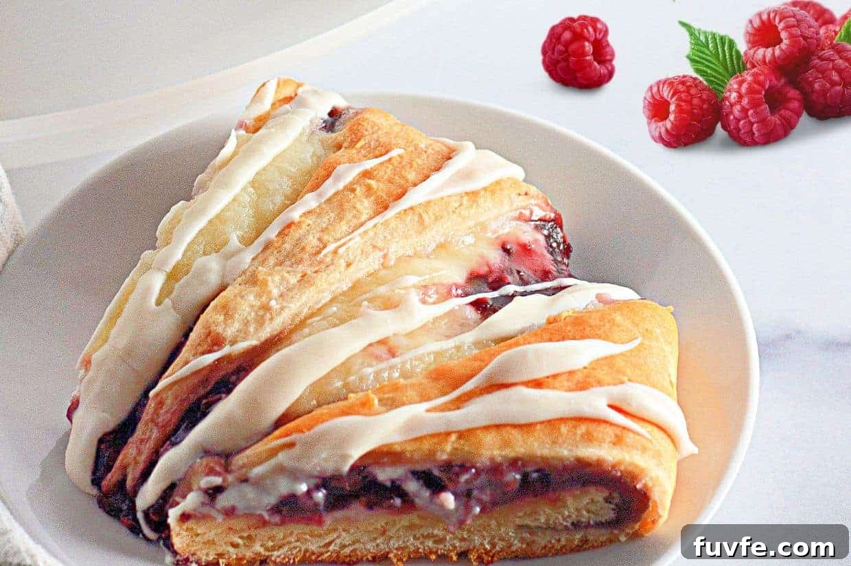 29 Christmas Baking Ideas for Home Bakers Who Love a Busy Oven 19 A slice of raspberry crescent ring with white icing on a white plate, with fresh raspberries and a green leaf in the background.
