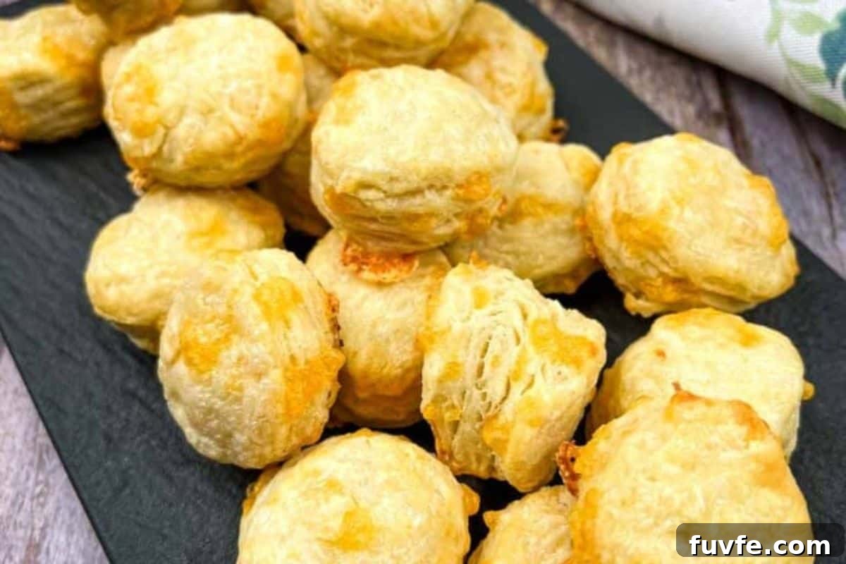 29 Christmas Baking Ideas for Home Bakers Who Love a Busy Oven 8 A plate of Mini Flaky Cheese Biscuits with raspberries, accompanied by a glass mug of coffee and a small bowl of yellow sauce on a white wooden table with a floral napkin.
