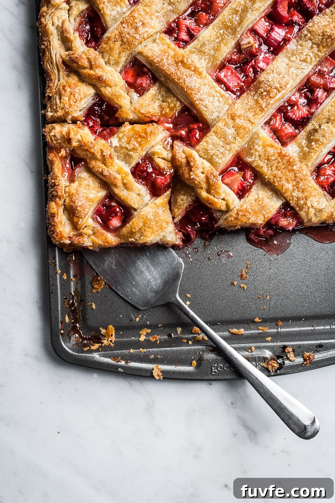 Strawberry Rhubarb Slab Pie Recipe — Perfect for Parties 2 Baked strawberry rhubarb slab pie with a piece cut and being lifted by a serving utensil