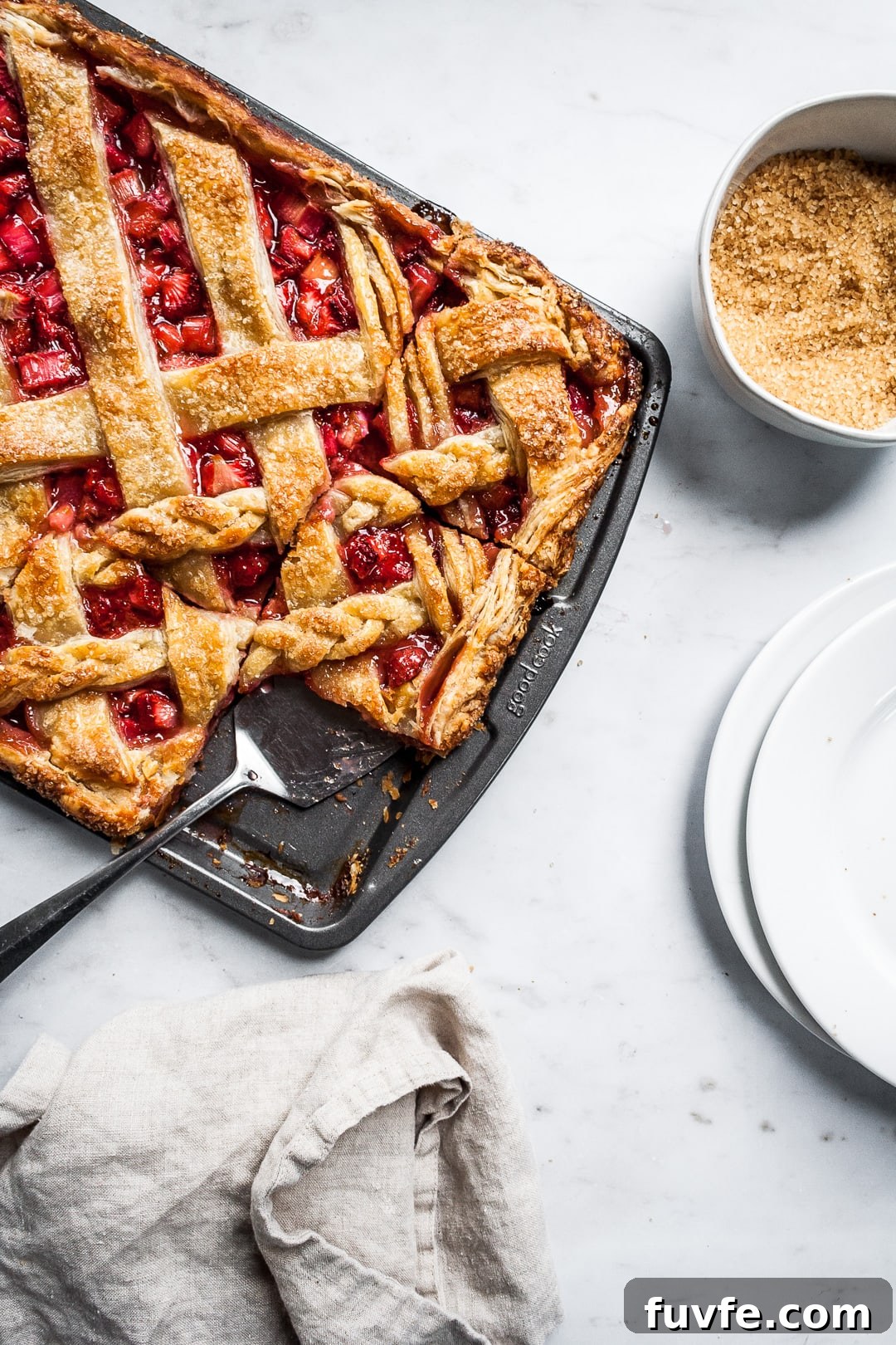 Strawberry Rhubarb Slab Pie Recipe — Perfect for Parties 12 Baked strawberry rhubarb slab pie in a sheet pan with several cut slices and a serving utensil on a marble background