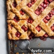 Strawberry Rhubarb Slab Pie Recipe — Perfect for Parties 13 A slice of strawberry rhubarb slab pie being cut out on a baking sheet.