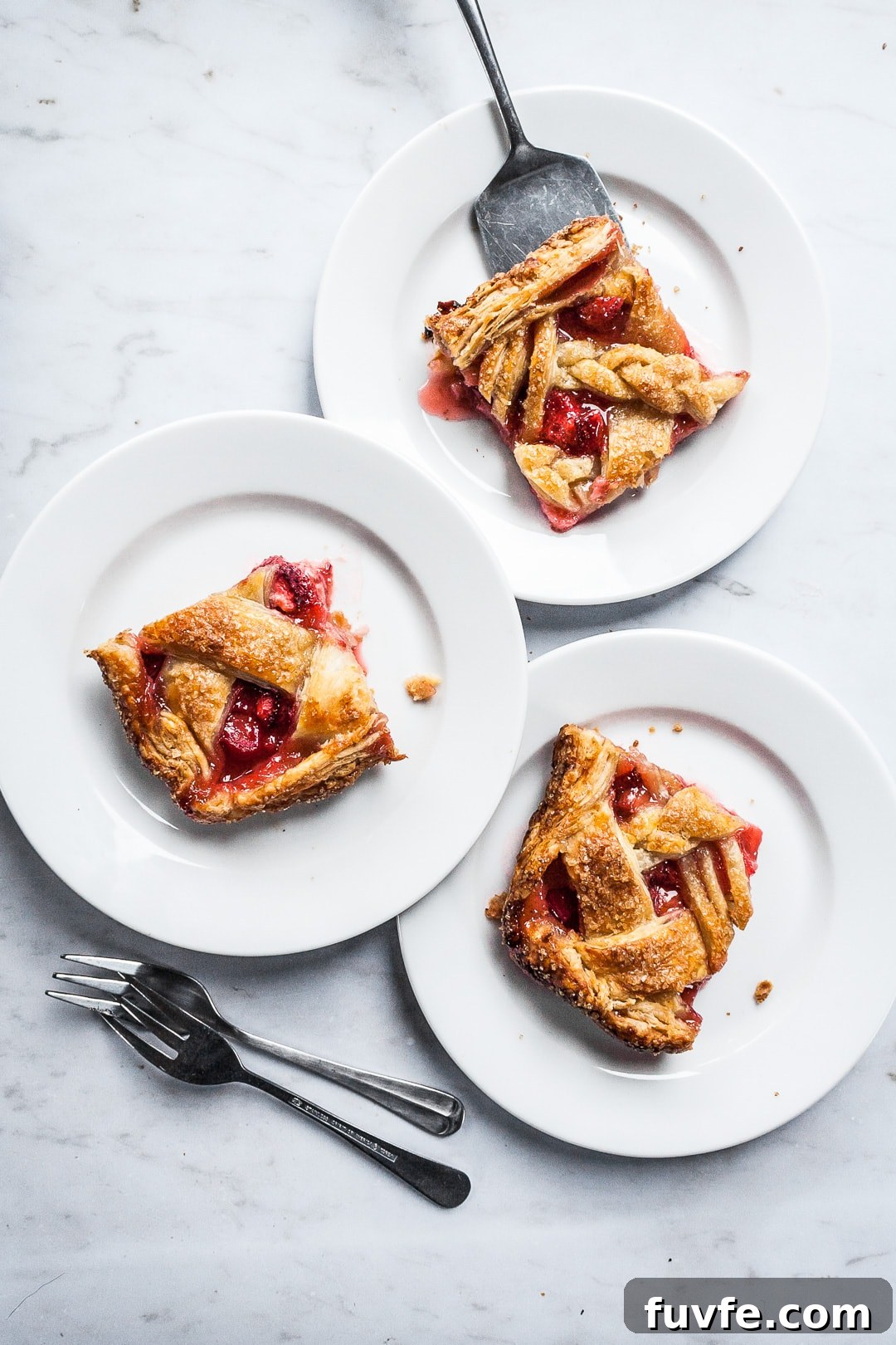 Strawberry Rhubarb Slab Pie Recipe — Perfect for Parties 15 Three square slices of slab pie on white plates and a marble background with forks and serving utensil nearby