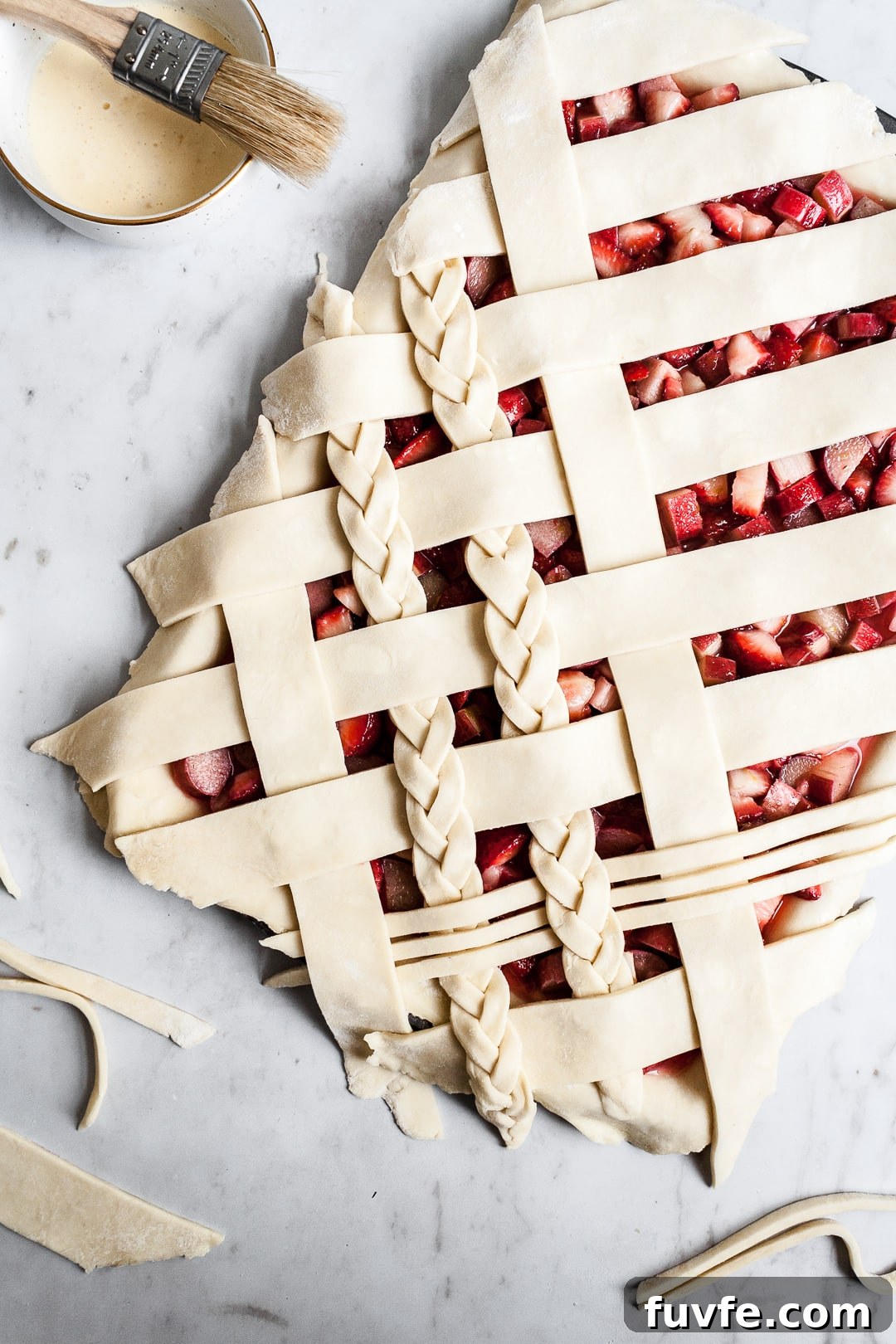 Strawberry Rhubarb Slab Pie Recipe — Perfect for Parties 4 Top view of unbaked strawberry rhubarb slab pie with angled woven lattice crust with braids on a white background