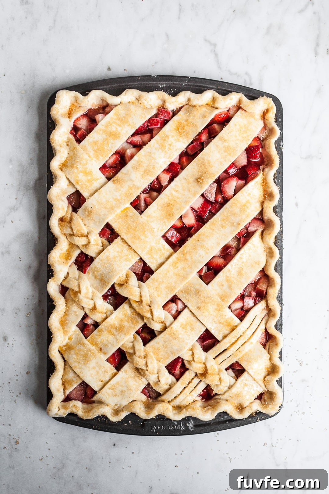 Strawberry Rhubarb Slab Pie Recipe — Perfect for Parties 6 Top view of unbaked crimped lattice slab pie with strawberry rhubarb filling, sprinkled with coarse sugar, on a marble background
