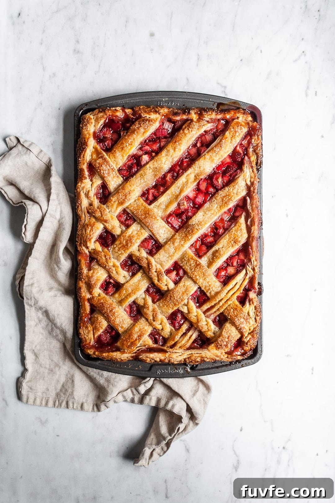 Strawberry Rhubarb Slab Pie Recipe — Perfect for Parties 7 Top view of baked strawberry rhubarb slab pie with natural linen towel underneath pan, resting on a marble background