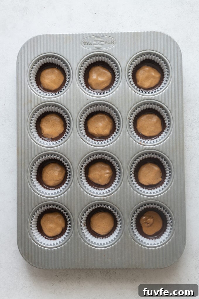 Muffin pan with peanut butter filling in dark chocolate for peanut butter cups.