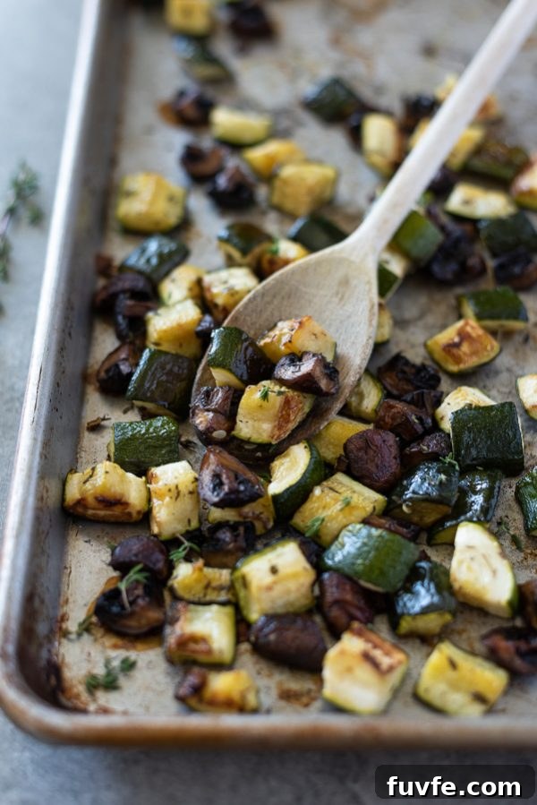 Garlic-Roasted Zucchini and Mushrooms Recipe 6 Roasted zucchini and mushrooms on a sheet pan with a wooden spoon