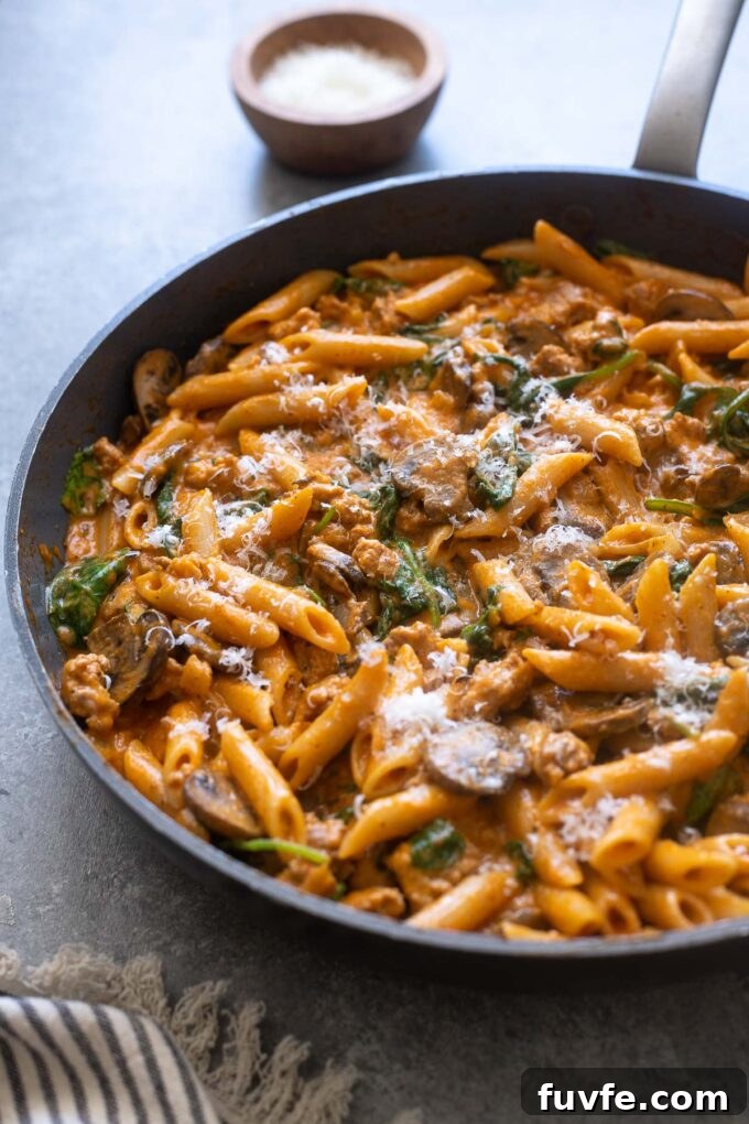 Creamy roasted red pepper pasta in a skillet topped with parmesan.