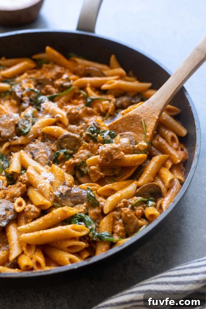 Sausage roasted red pepper pasta in skillet with wooden spoon.