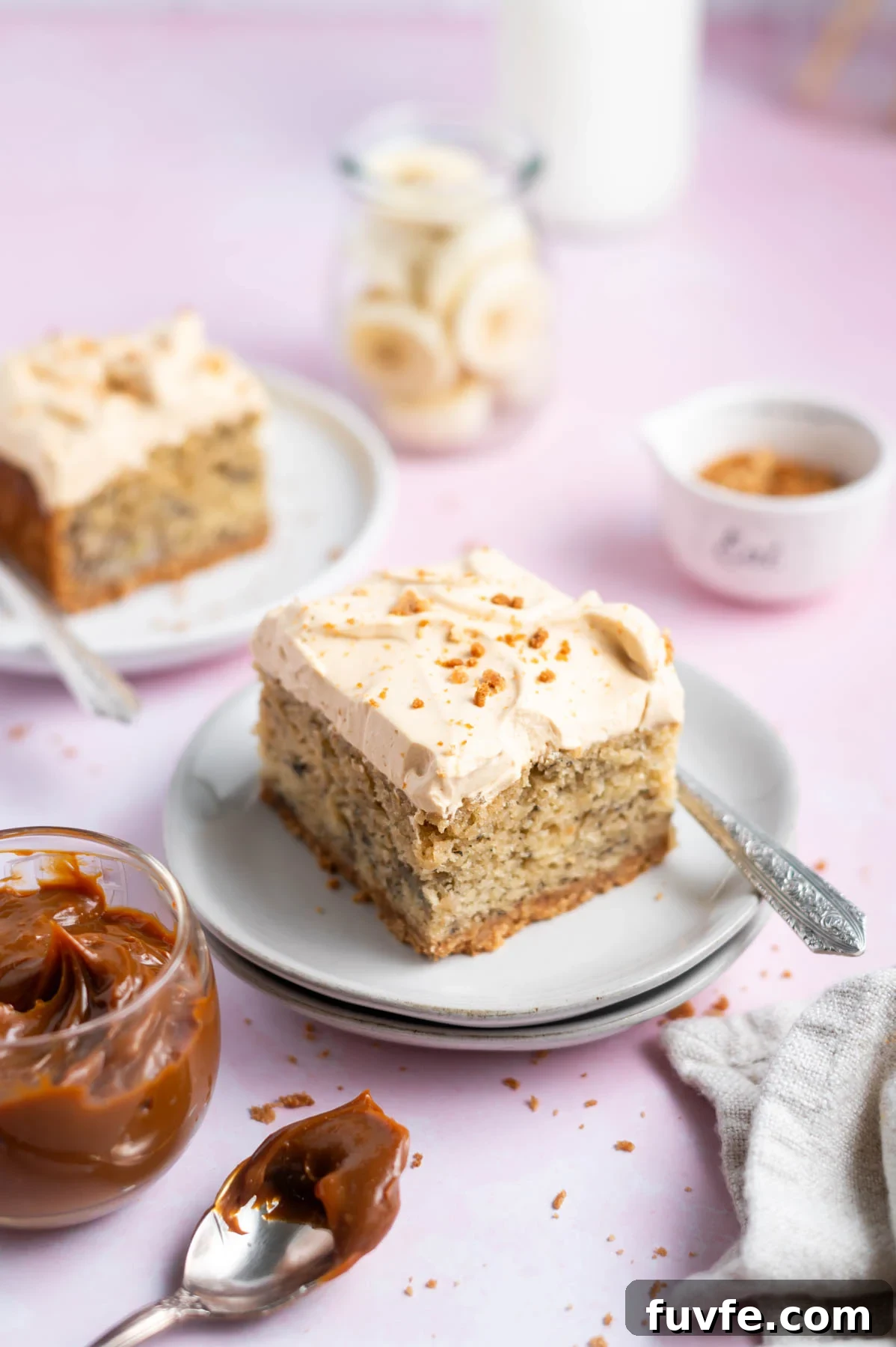 Decadent Banoffee Cake Recipe with Caramelized Banana Layers 2 slices of cake on plate with forks and a bowl of dulce de leche