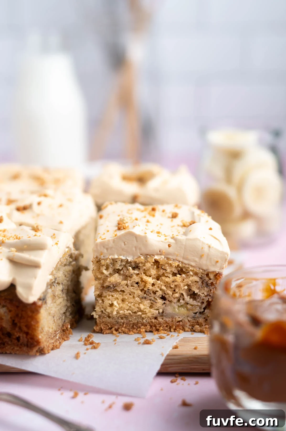 Decadent Banoffee Cake Recipe with Caramelized Banana Layers 16 slice of banoffee cake on a cutting board with banana slices in the background and a jar of dulce de leche