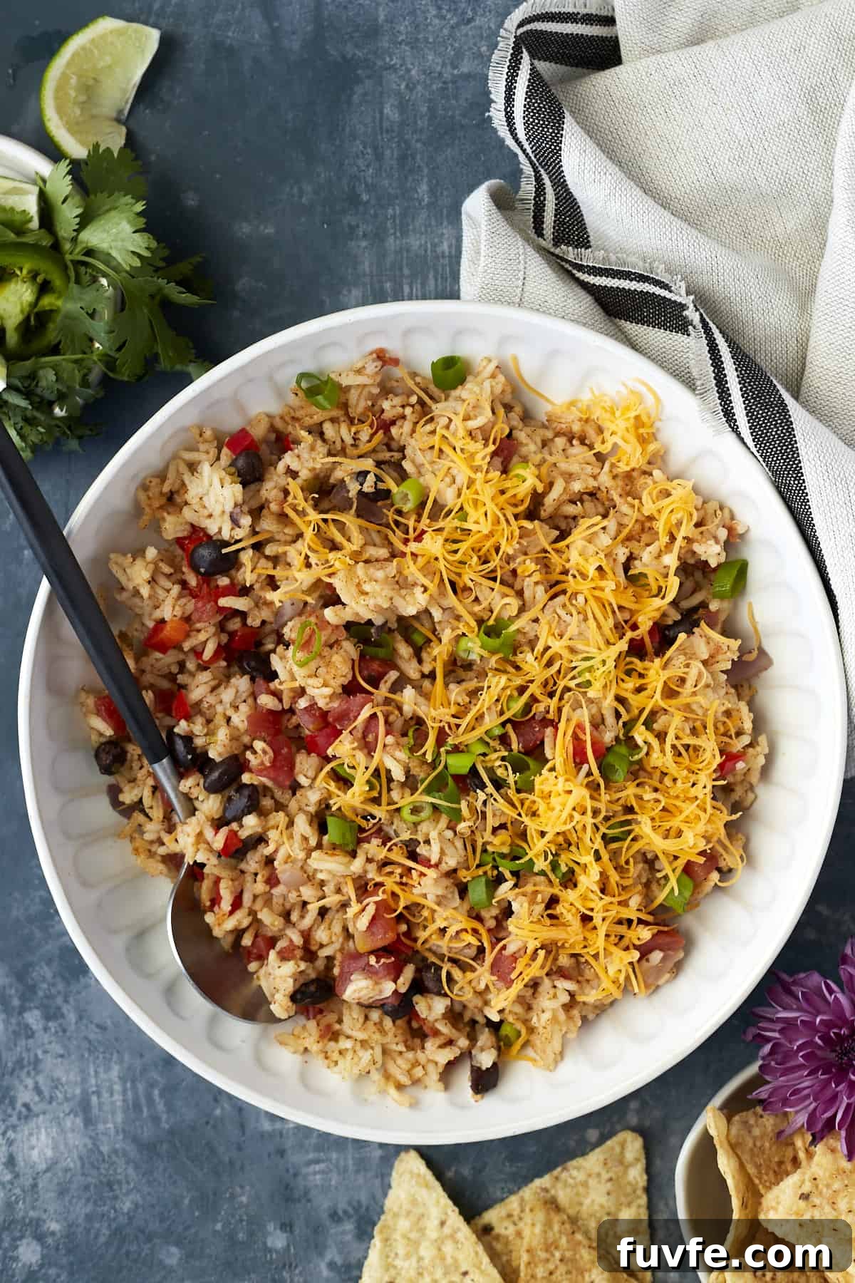 Overhead image of a white plate full of easy Mexican rice recipe with veggies and cheese with a black spoon on the side