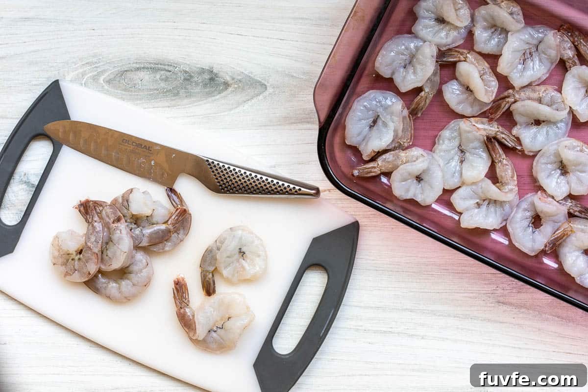 Oven-Baked Stuffed Shrimp with Garlic Herb Breadcrumbs 5 shrimp on cutting board with knife next to baking dish with butterflied shrimp.