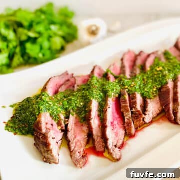 spicy chimichurri sauce over sliced steak with fresh cilantro and garlic in the background