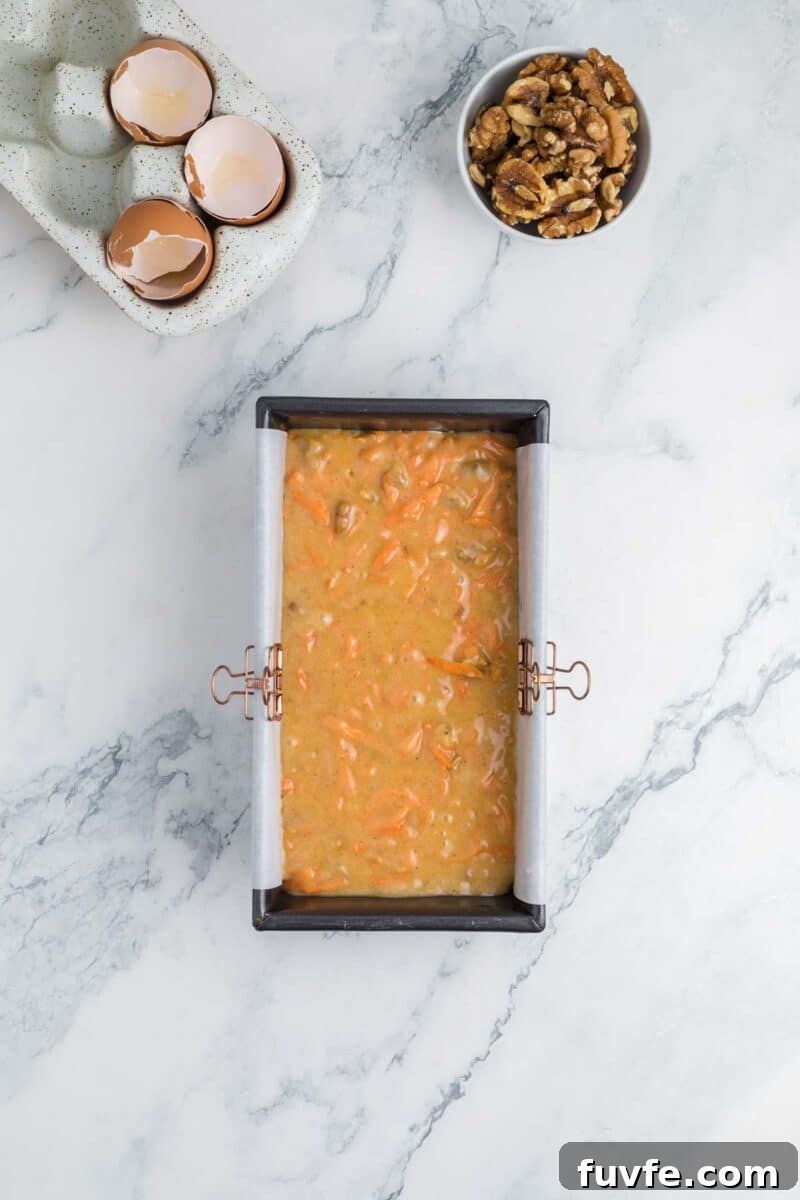 A loaf pan filled with carrot cake batter sits on a marble surface.