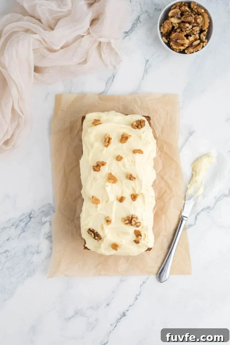 A loaf cake with white frosting and walnut halves on top sits on parchment paper.