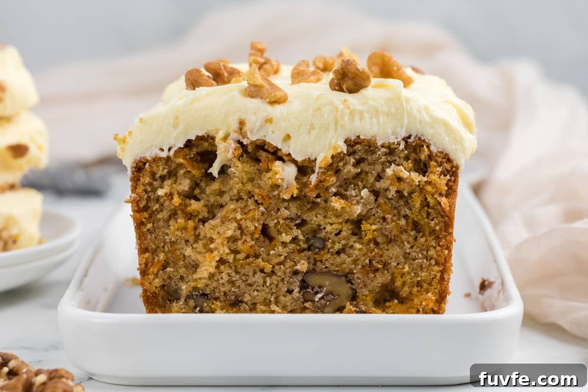 A sliced loaf of carrot cake with cream cheese frosting and walnut pieces on top, displayed on a white rectangular plate.