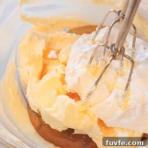 A hand mixer sits in a glass bowl filled with butter, honey, and marshmallow cream.