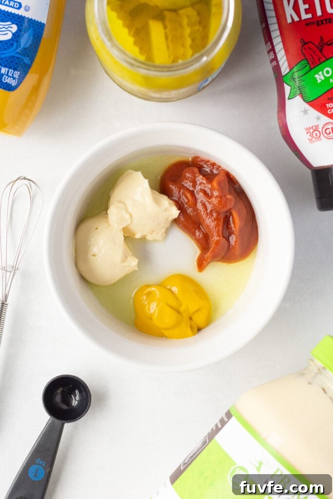 Quick 4-Ingredient Burger Sauce Recipe for Classic Flavor 4 Top down shot of ingredients for burger sauce in a small white dish surrounded by bottles and jars of ketchup, mayo, yellow mustard, and dill pickles.