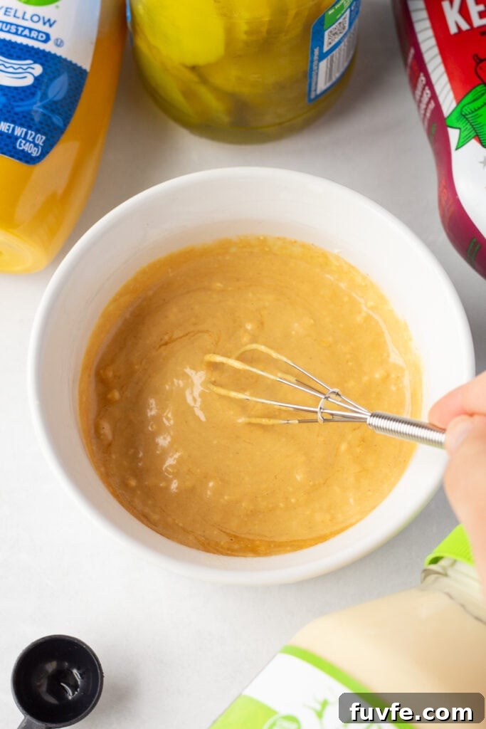 Quick 4-Ingredient Burger Sauce Recipe for Classic Flavor 5 Close up of a hand using a small whisk to stir a golden sauce in a small white dish.