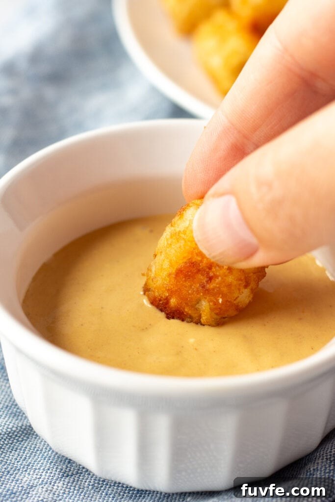 Quick 4-Ingredient Burger Sauce Recipe for Classic Flavor 7 Close up of a hand dipping a tater tot into a golden burger sauce in a small white dish.