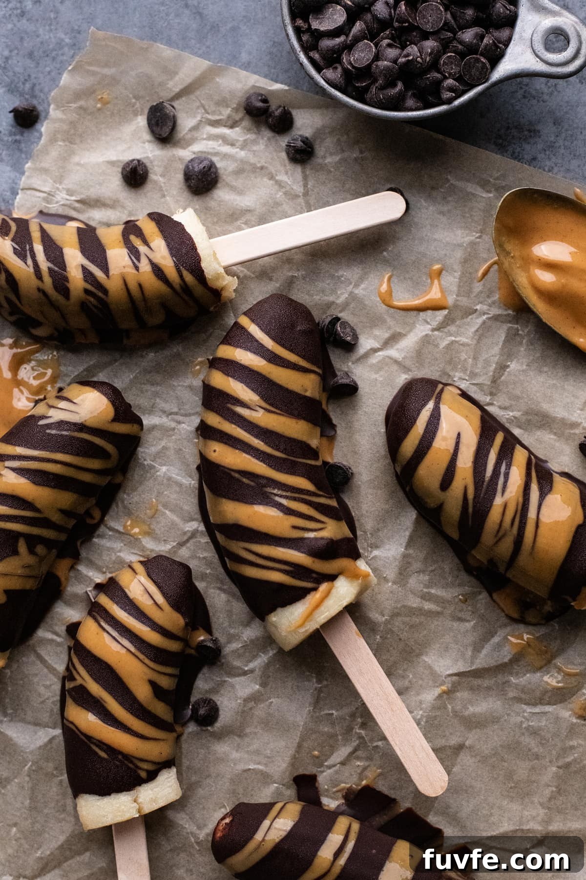 chocolate covered frozen bananas arranged on parchment paper with peanut butter drizzled over top.