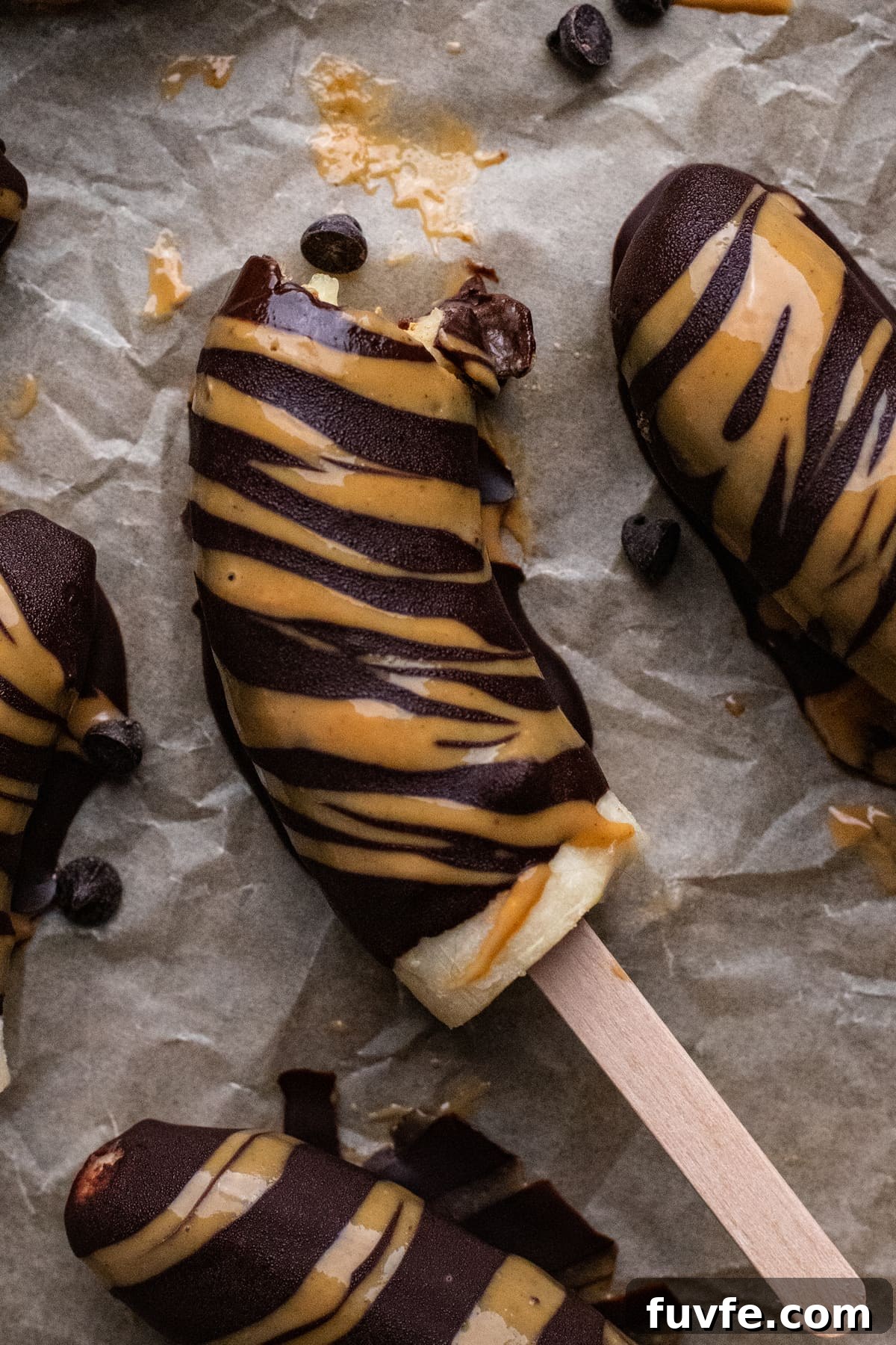frozen chocolate covered banana drizzled with peanut butter on parchment paper.