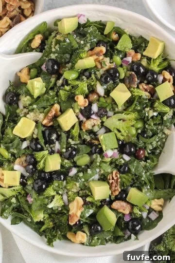 Superfood salad with blueberries, broccoli, walnuts, and avocado in a white serving bowl with white salad utensils.