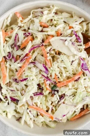 Creamy coleslaw in a serving bowl with a gold spoon.