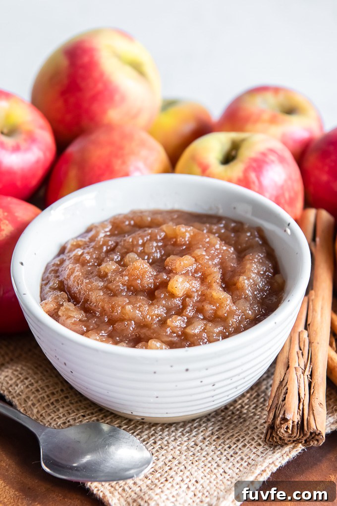 Homemade applesauce in a white bowl with cinnamon sticks and apples