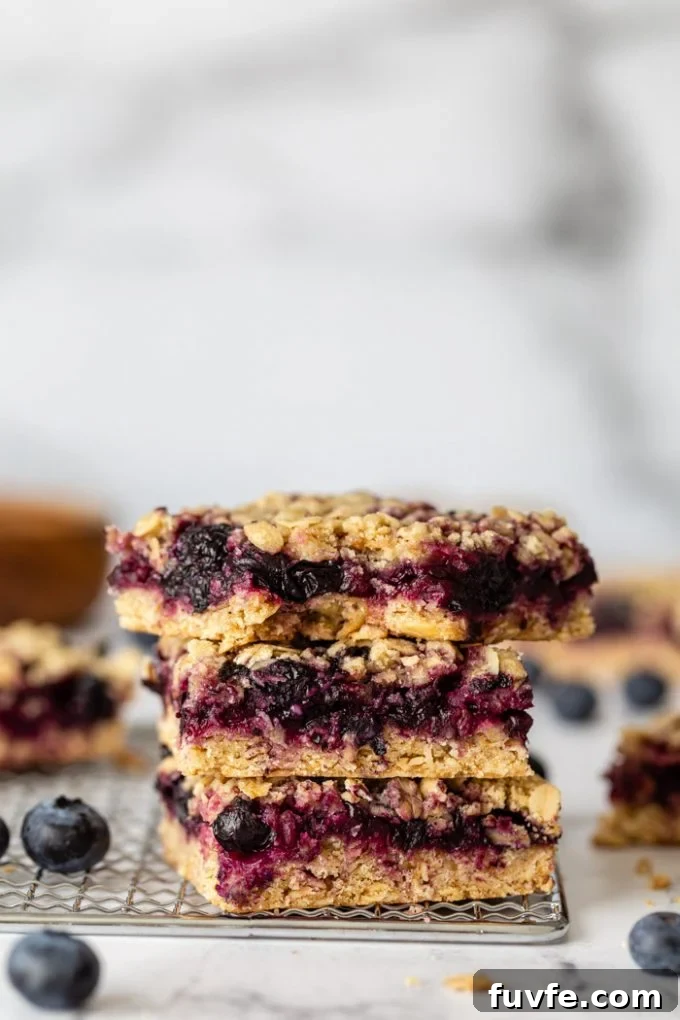 Chewy Blueberry Crumble Bars with Golden Oat Topping 4 stack of blueberry crumble bars on a silver rack with blueberries around