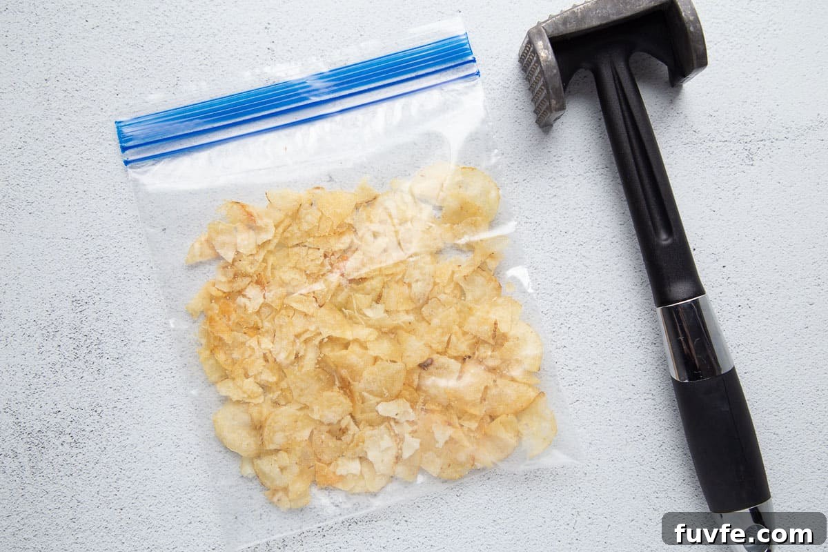 plastic bag full of potato chips next to a meat mallet.